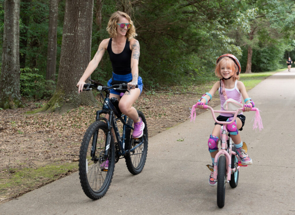 Mother and daughter riding bikes on a paved trail through the forest