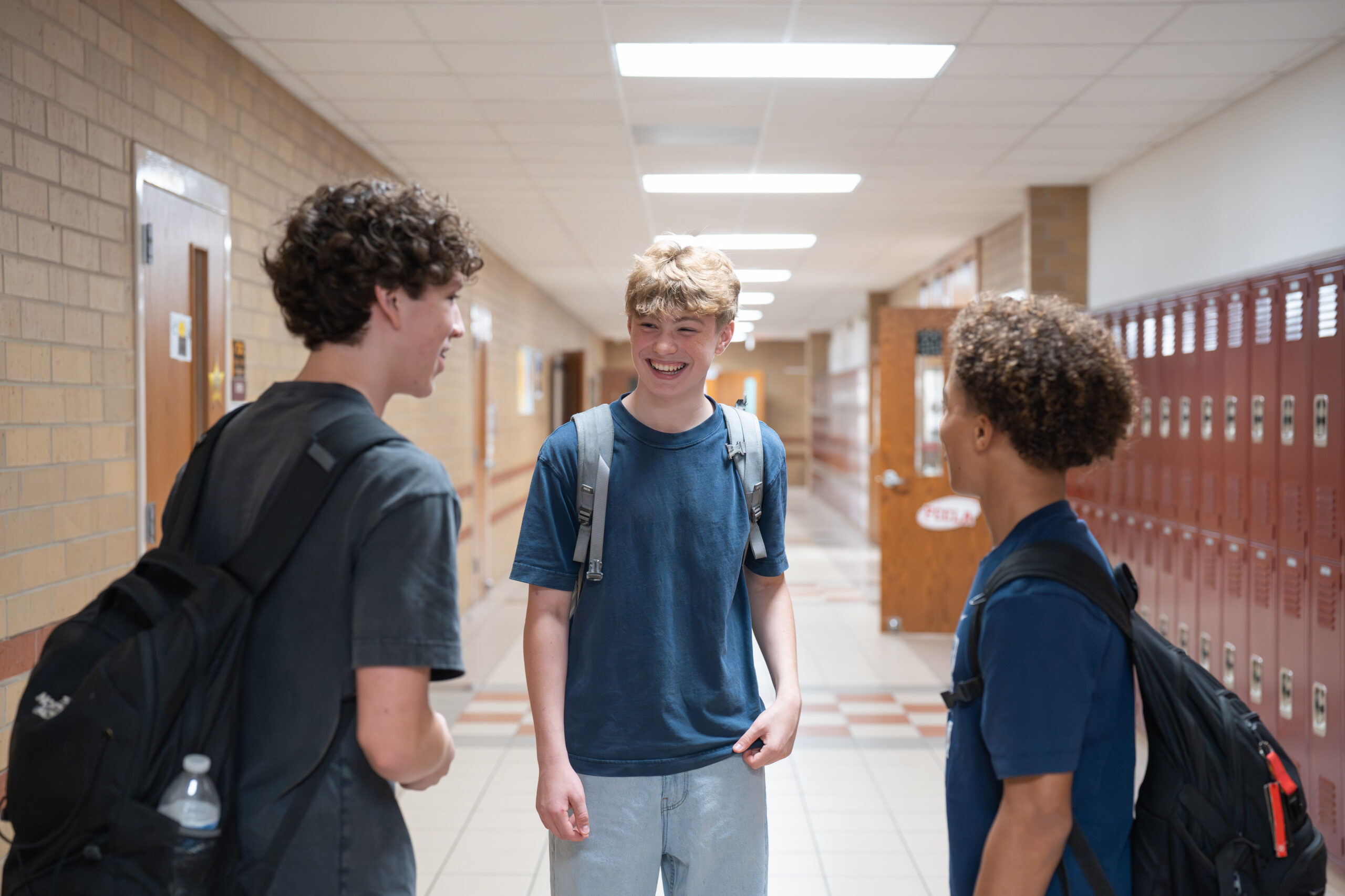 Three teenage boys standing in a school hallway