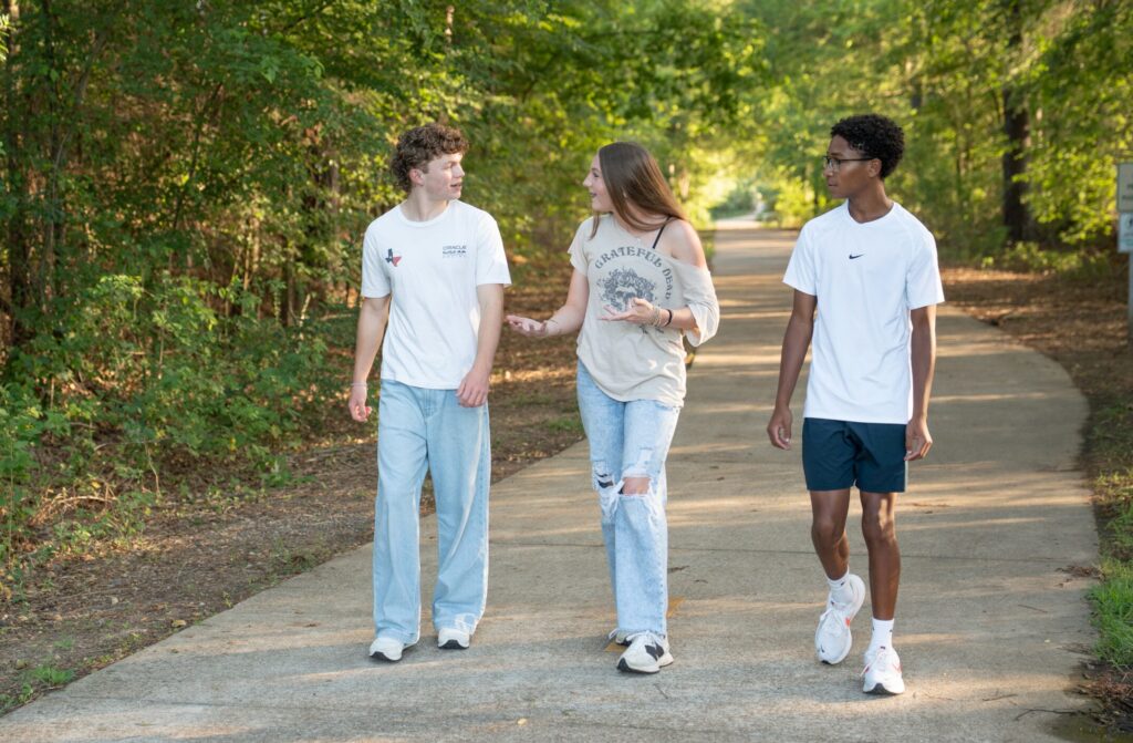 Three teens walking along a path surrounded by trees.
