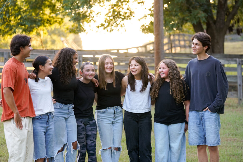 Group of teenagers standing together in a line with their arms on each others backs.